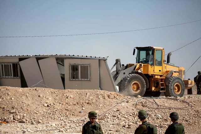 A bulldozer belonging to Israeli authority demolishes three building of Palestinians in the Masafer Yatta neighbourhood of southern Hebron, West Bank on August 14, 2017, under the observation of Israeli forces. (Photo by Mamoun Wazwaz / Anadolu Agency / Getty Images)