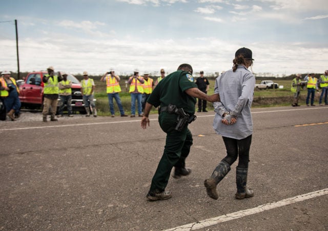 A protester arrested during a sit-in at a Bayou Bridge Pipeline construction site is lead past pipeline workers. Environmentalists say oil companies should hire more workers to fix leaky and aging fossil fuel infrastructure in Louisiana rather than building new pipelines. (Photo: © 2018 Julie Dermansky)
