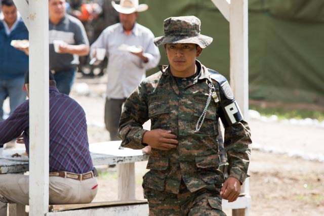 Workers from the construction site of a Cementos Progreso access road eat as a soldier walks to meet with journalists. (Photo: Jeff Abbott) 