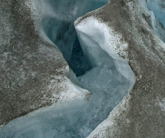 An ice sheet drain or moulin carries melt water into the depths of the ice sheet through crevasses. This image illustrates how little of the accumulated dust on the ice sheet washes away with melt runoff. (Photo: Bruce Melton)