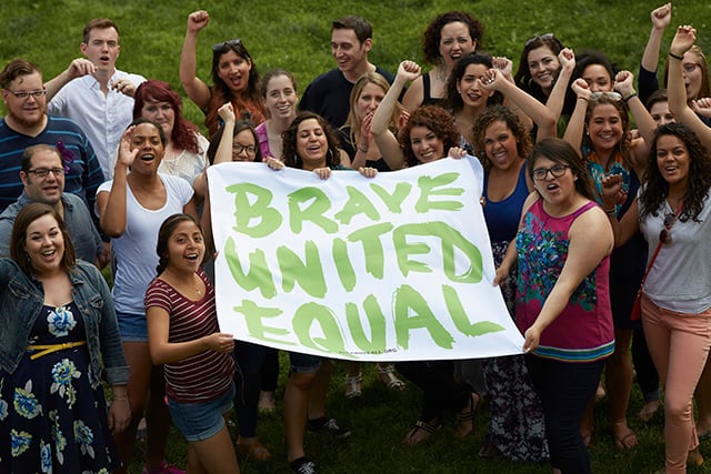 The video participants cheering together with the sign they made of All* Above All’s slogan: “Brave United Equal.” (Photo: All* Above All)