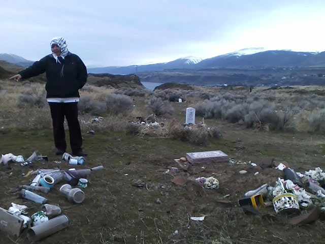Lana Jack at the Celilo Wy'am's relocated burial site, on a hill above the drowned Celilo Falls. Jack points to the grave of a recent ancestor, January, 2016. (Photo: Simon Davis-Cohen)