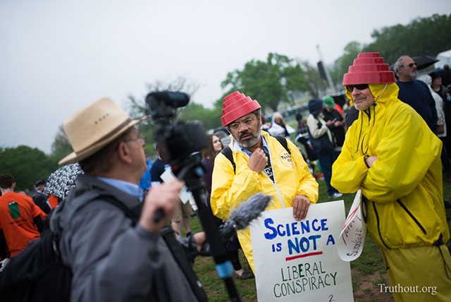 Two men are interviewed wearing Devo hats and yellow jumpsuits, creative outfits at the march included anything from white lab coats to cartoon characters. (Photo: Zach Roberts) 