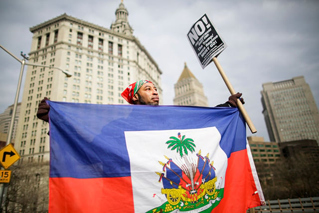 A man holds a Haitian flag as people take part in a protest against Donald Trump's recent statements and words about immigration crossing the Brooklyn Bridge on January 19, 2018, in New York City. (Photo: Eduardo MunozAlvarez / VIEWpress/Corbis via Getty Images)