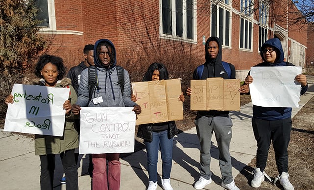 Students at Sullivan High School begin gathering outside their school before a neighborhood march. One of the students holds a sign that reads, 