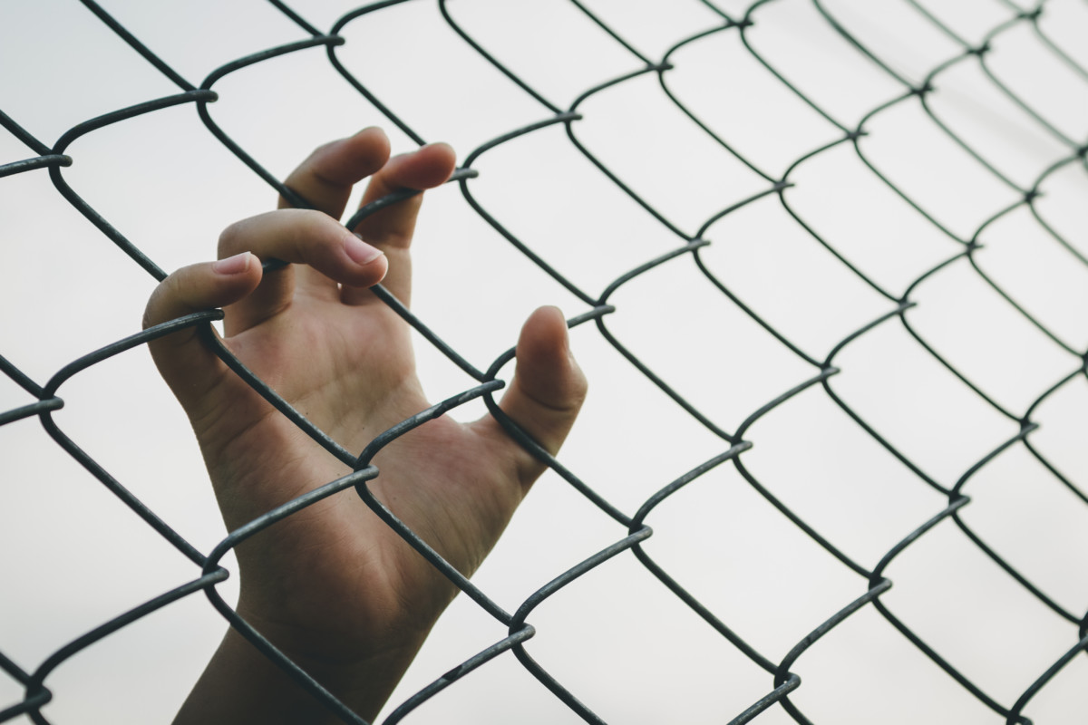 Youth's hand grasping fence