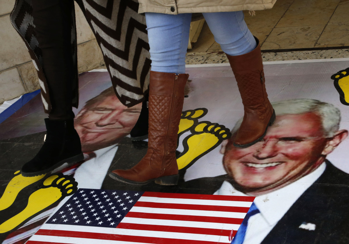 Palestinians walk on a poster bearing images of Donald Trump and his deputy Mike Pence during a demonstration at the al-Quds Open University in Dura village on the outskirts of the West Bank town of Hebron on December 13, 2017.