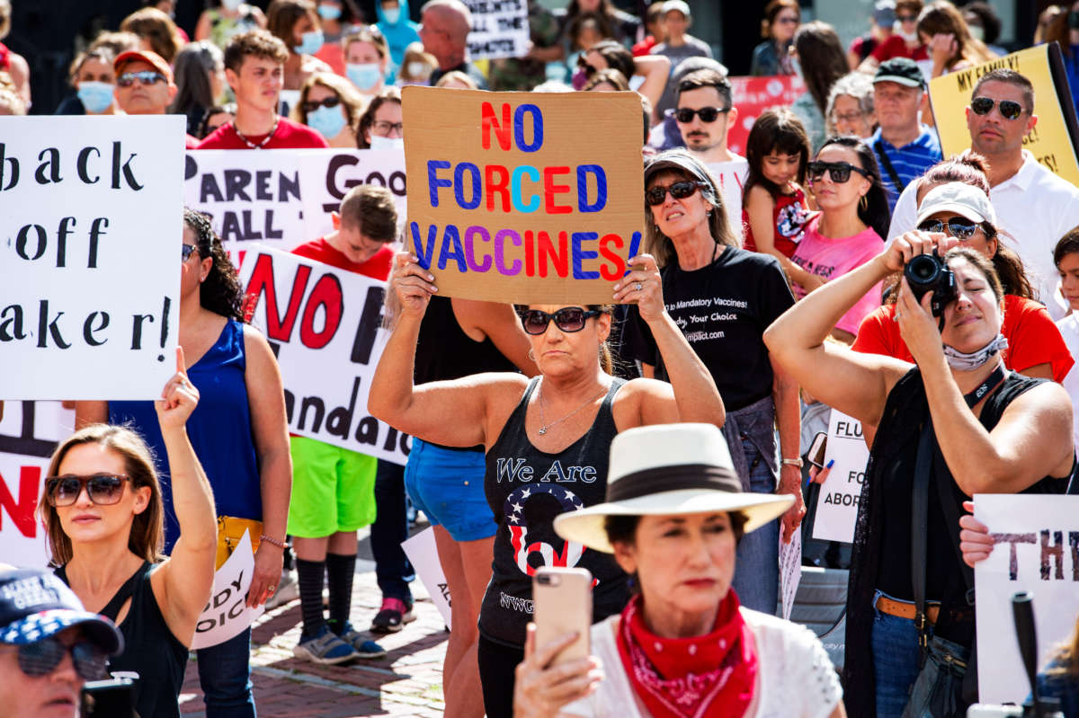 A woman with a QAnon shirt and a "no forced vaccines" sign stands with protesters outside the Massachusetts State House in Boston on August 30, 2020.