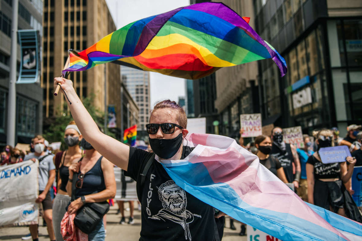 A marcher waves the trans and gay pride flags at a protest