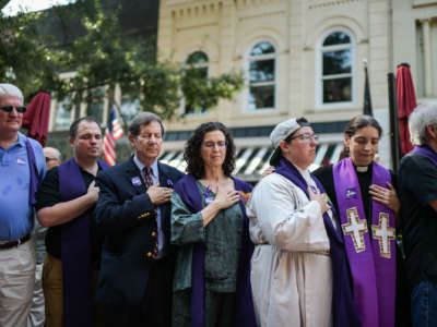 members of the clergy in purple pray at an outdoor, pre-covid vigil