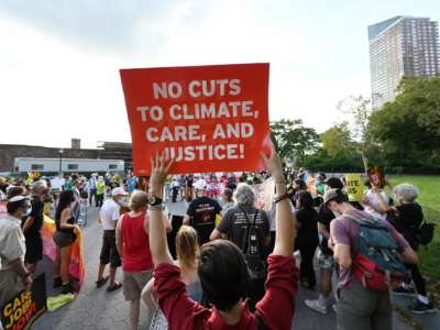 A protester holds a sign reading "NO CUTS TO CLIMATE, CARE AND JUSTICE!" during a demonstration