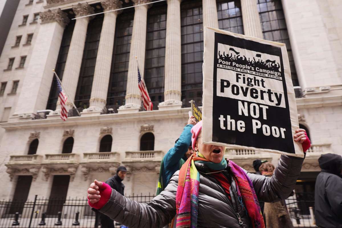 A person holds a sign reading "FIGHT POVERTY, NOT THE POOR" during an outdoor, pre-covid protest