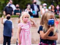 A little girl in a mask that matches her dress gives someone a thumbs up