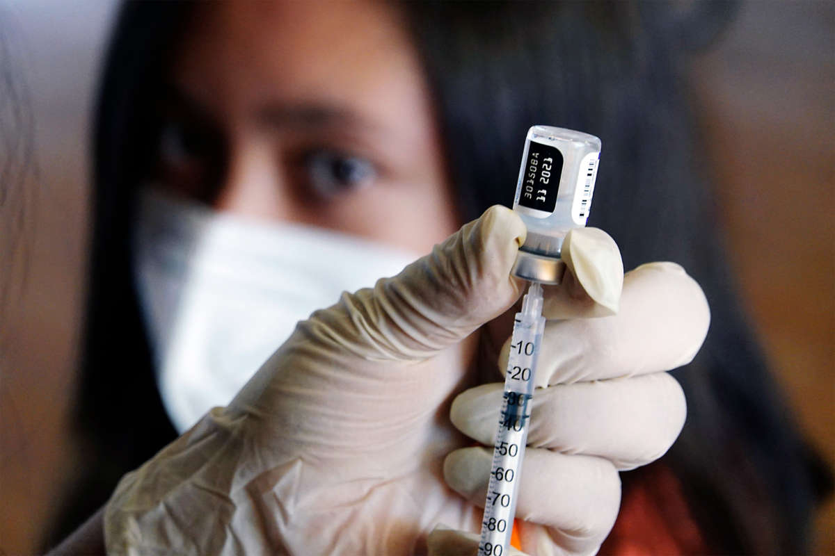A medical worker fills a syringe with the pfizer/biontech vaccine as their patient looks onward in the background
