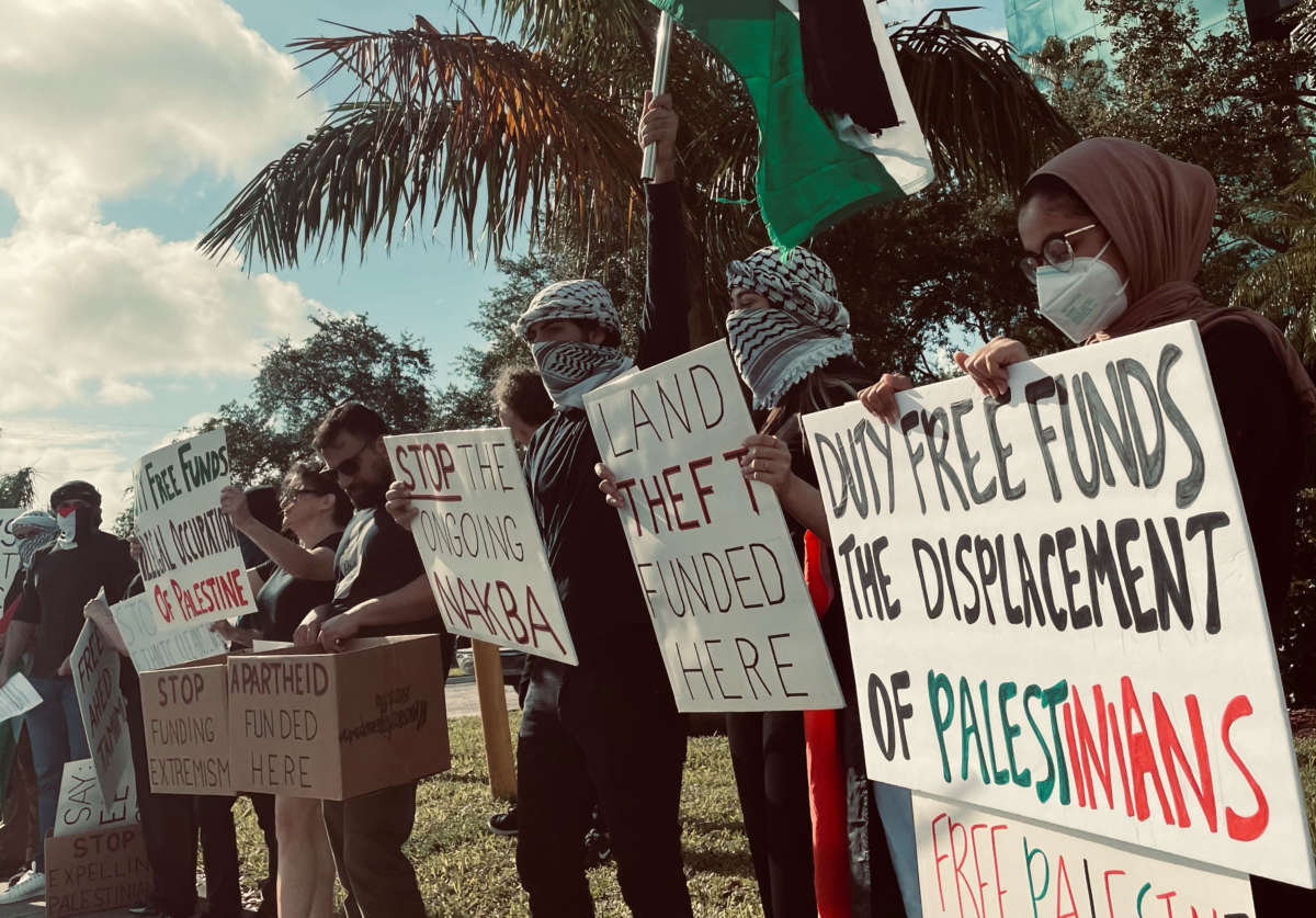 Protesters hold signs in front of the Duty Free Americas headquarters in South Florida.