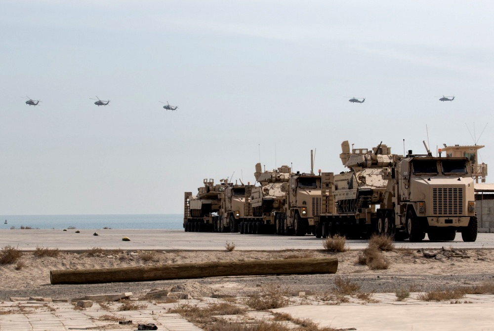 UH-60 Black Hawk helicopters fly over armored vehicles that have been loaded onto trucks for transport on February 9, 2018, at the Kuwait Naval Base.