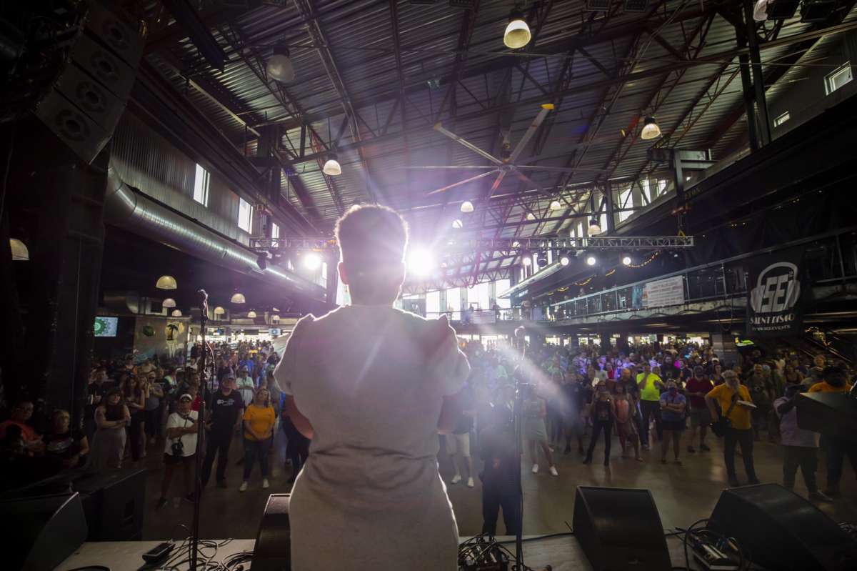 A woman is silhouetted by a spotlight as she speaks to a crowd of supporters from a stage