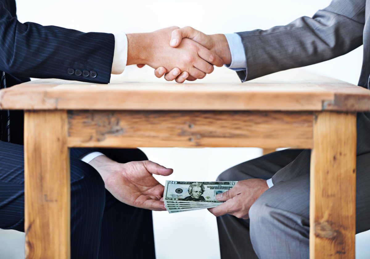 Cropped shot of two businessmen shaking hands while money passes hands under a table