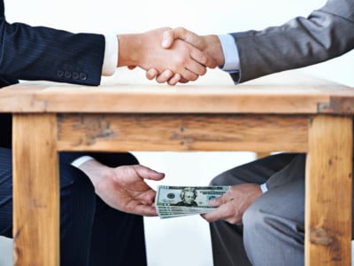 Cropped shot of two businessmen shaking hands while money passes hands under a table