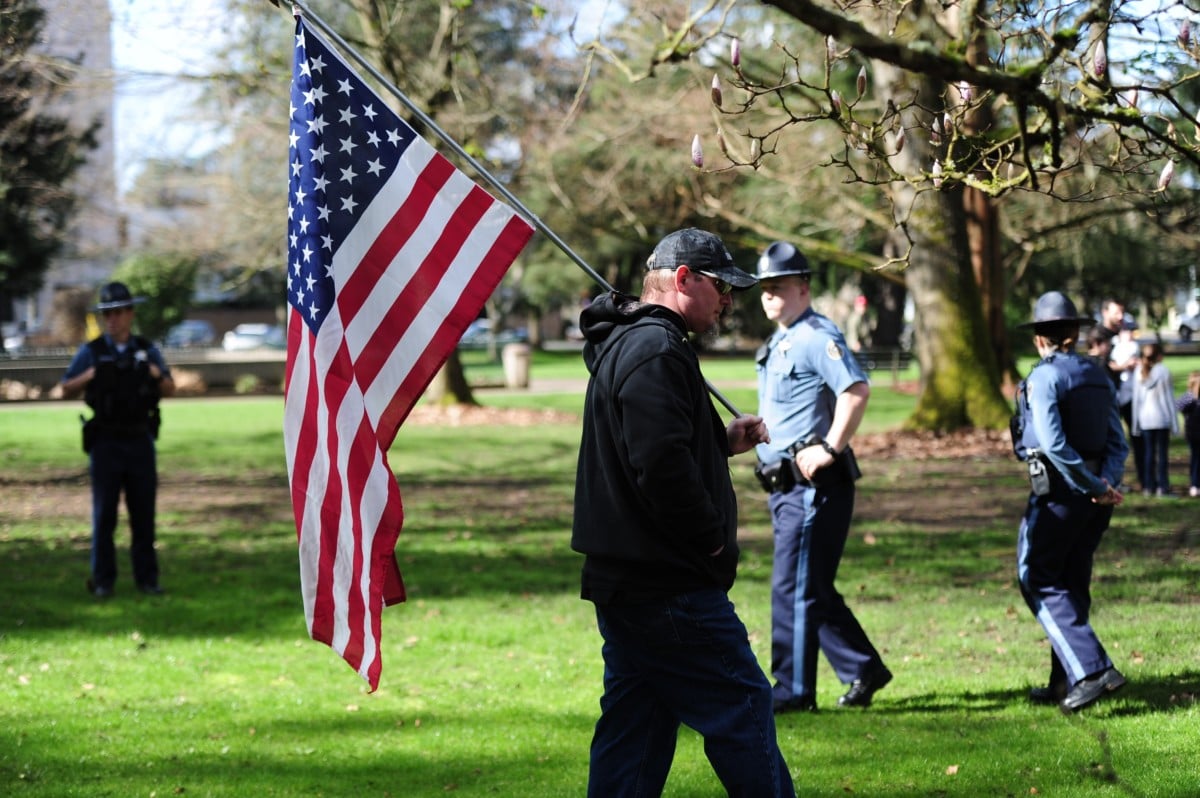 A Trump supporter carries an American flag as police monitor the scene during a "Make America Great Again" rally in Salem, Oregon, on March 25, 2017.