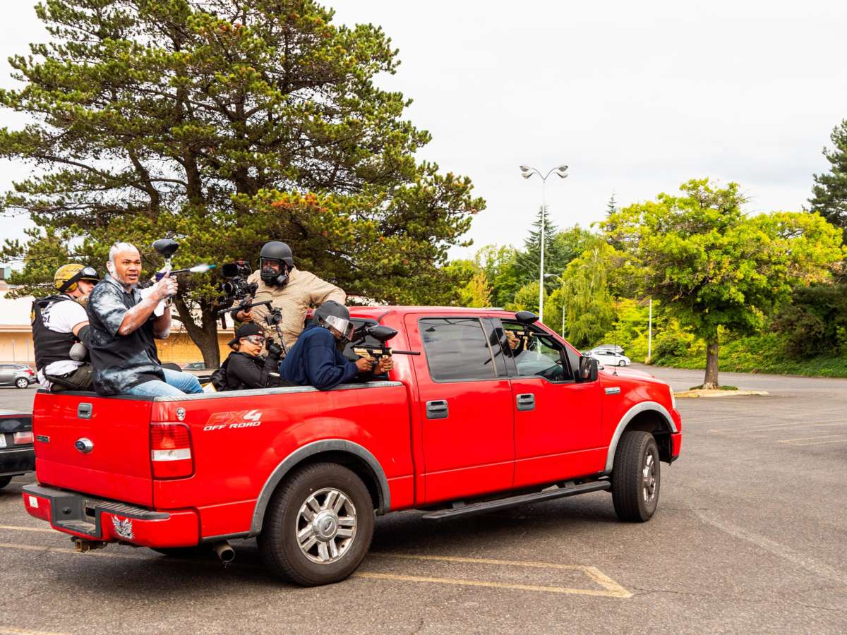 Men shoot guns from the back of a red pickup truck