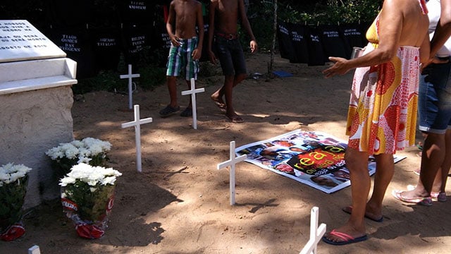 Residents look down on the 12 white crosses and a memorial banner at the site where 12 black men were killed in the Cabula Massacre. (Photo: Lena Azevedo)