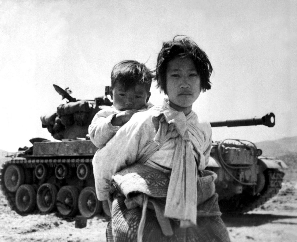 Carrying her baby brother on her back, a war weary Korean girl walks by a stalled M-26 tank, at Haengju, Korea, June, 1951.