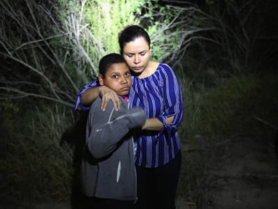 A US Border Patrol spotlight shines on a terrified mother and son from Honduras as they are found in the dark near the US-Mexico border on June 12, 2018, in McAllen, Texas. The asylum seekers had rafted across the Rio Grande from Mexico and had become lost in the woods. They were then detained by Border Patrol agents and then sent to a processing center for possible separation.