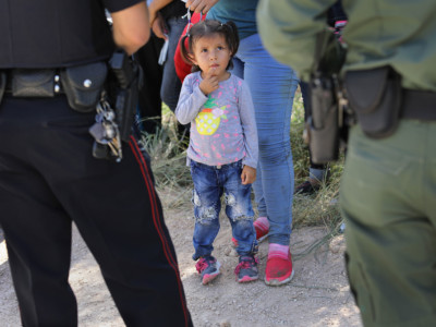 A Mission Police Dept. officer and a US Border Patrol agent watch over a group of Central American asylum seekers before taking them into custody on June 12, 2018 near McAllen, Texas.
