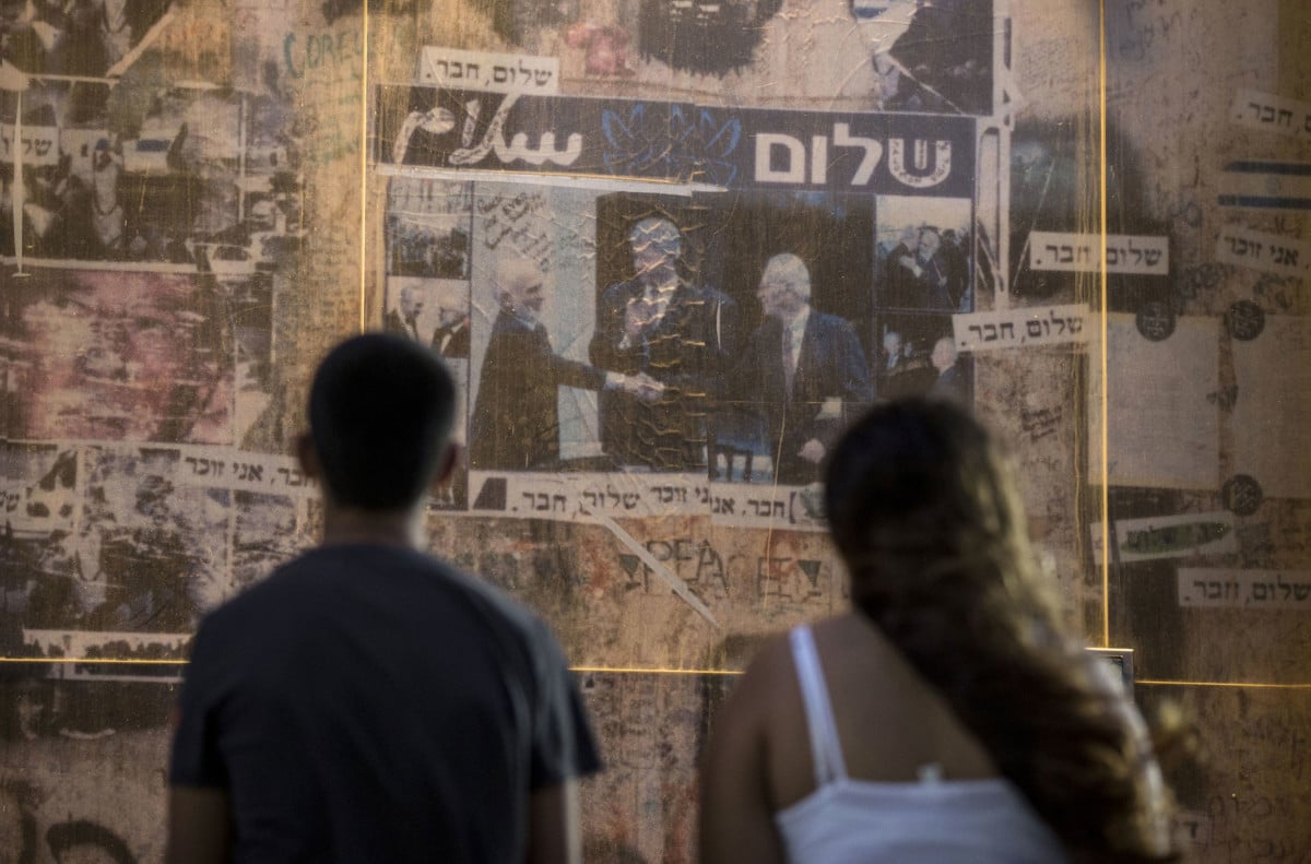 People look at a 20-year-old picture of late Israeli Prime Minister Yitzhak Rabin (right) shaking hands with late Jordanian King Hussein (left) while former President Bill Clinton applauds, framed by the words "peace" in Arabic and Hebrew. The photo is a memorial in the place where Rabin was assassinated in the Israeli Mediterranean city of Tel Aviv in 1995.
