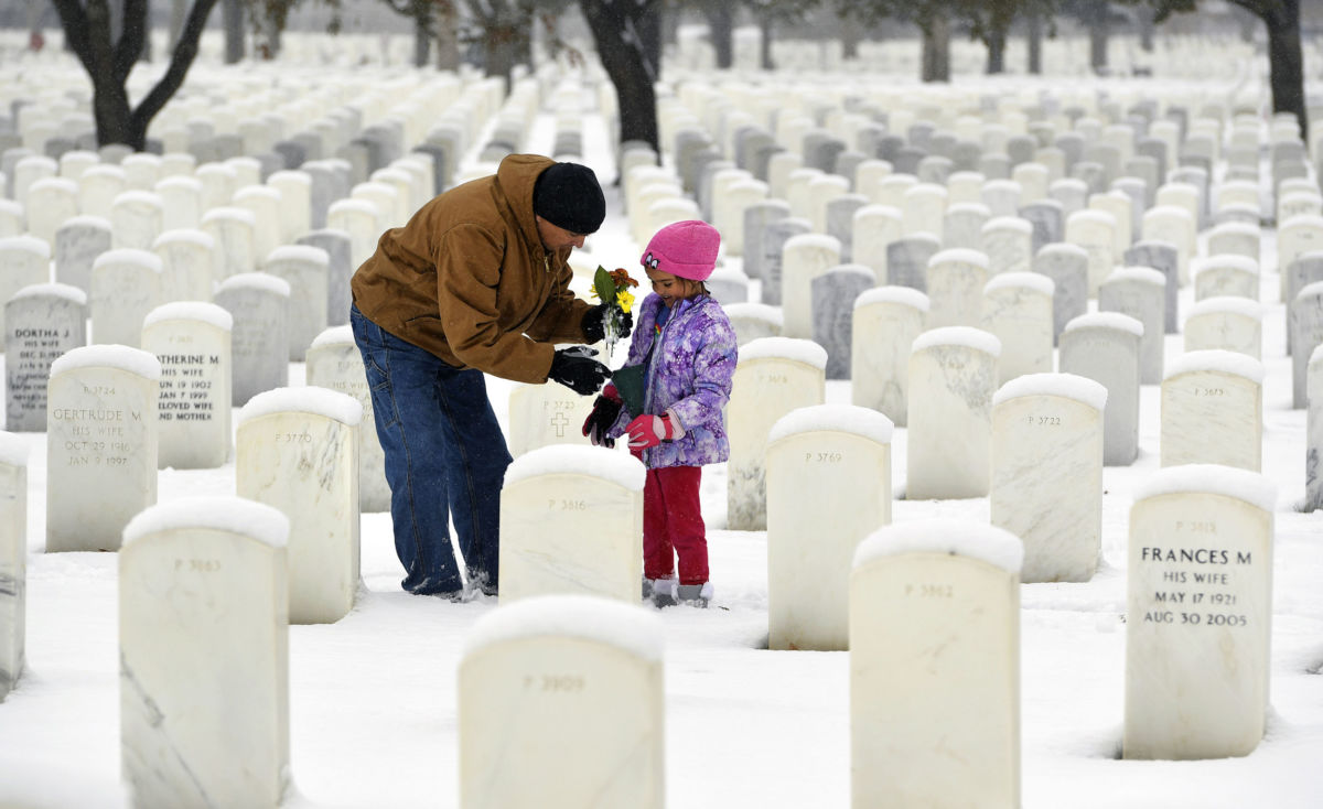 A father helps his daughter hold flowers before putting them onto headstones of family members after the Fort Logan VA National Cemetery Veterans Day Ceremony at Fort Logan National Cemetery on November 11, 2018, in Denver, Colorado.