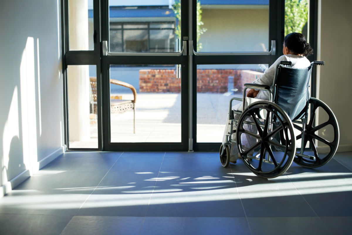 Elderly patient sits in a wheelchair near a hospital entrance