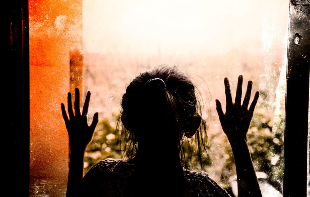 Girl in silhouette with hands against window.