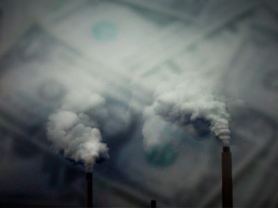 Two smokestacks billow smoke into a hazy gray sky with U.S. dollars in the background