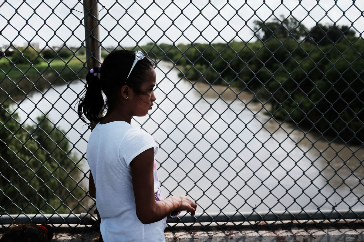 A young girl stands outside a chain link fence