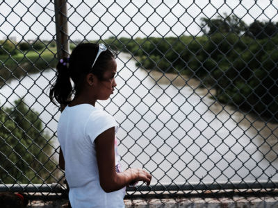 A young girl stands outside a chain link fence