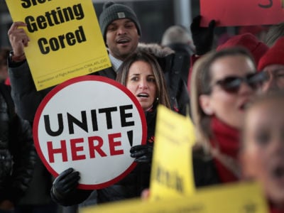 A woman holds a sign that reads "UNITE HERE" during a protest
