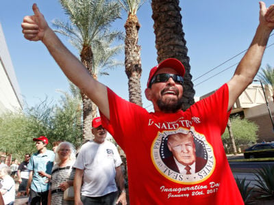 A man in a red shirt with Donald Trump's face on it yells while giving thumbs up