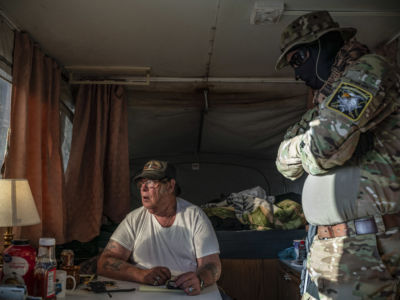 Two men sit speak to eachother while inside of a camper