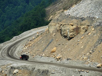 A dumptruck drives up a mined mountain as a forest is seen in the background