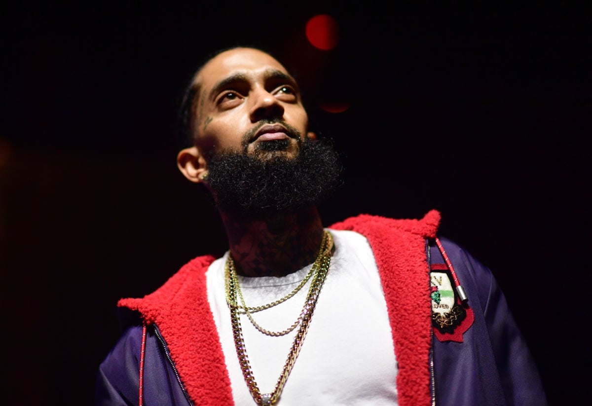 Nipsey Hustle stands in a darkened environment