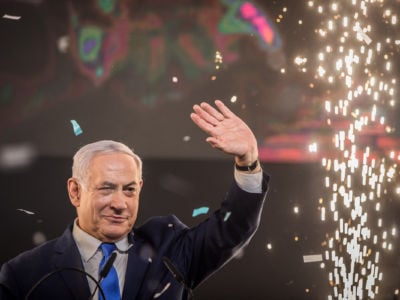 Benjamin Netanyahu raises a hand as sparks fly behind him