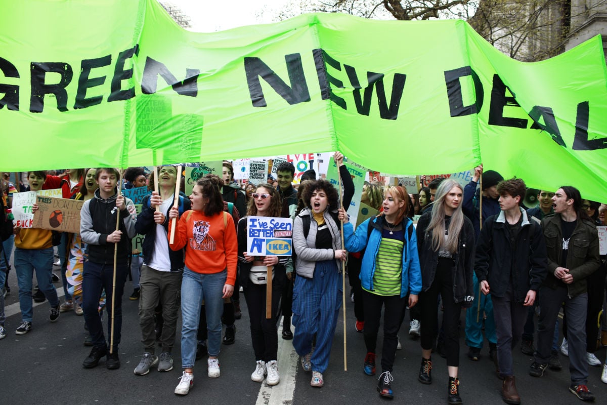 Young adults carry a green "GREEN NEW DEAL" sign during a large protest