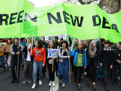 Young adults carry a green "GREEN NEW DEAL" sign during a large protest