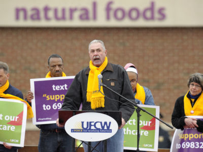 A man speaks at a podium surrounded by other protesters