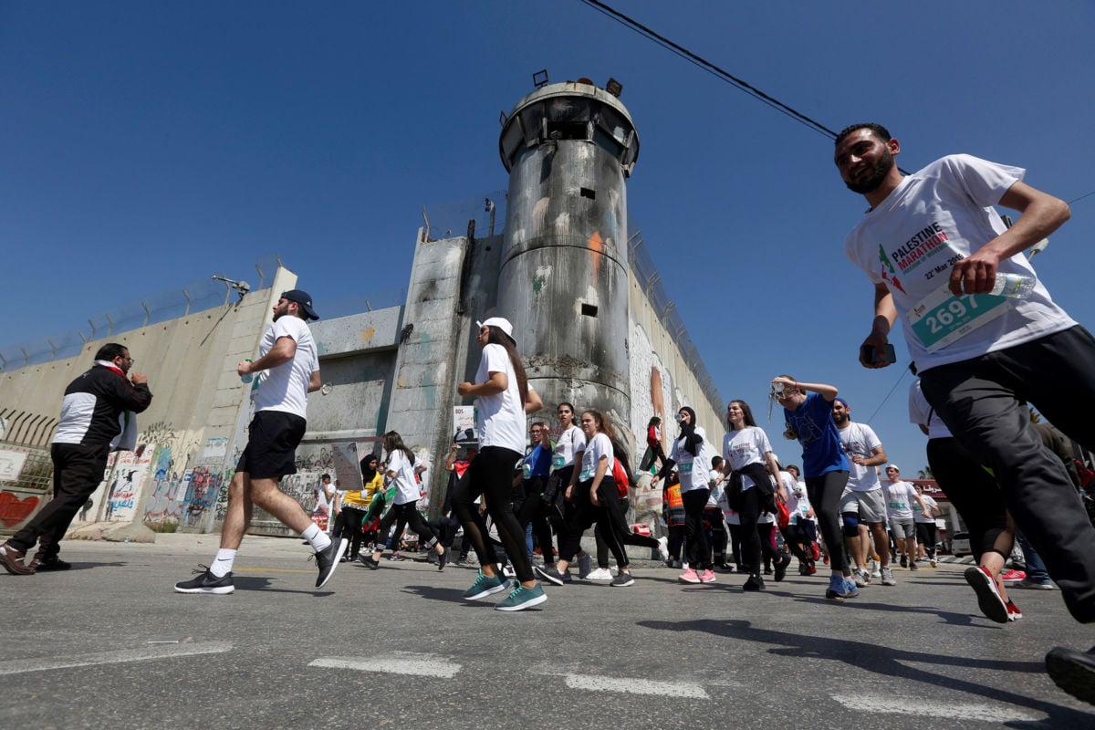 Runners in the Palestine Marathon pass a guard tower and border wall