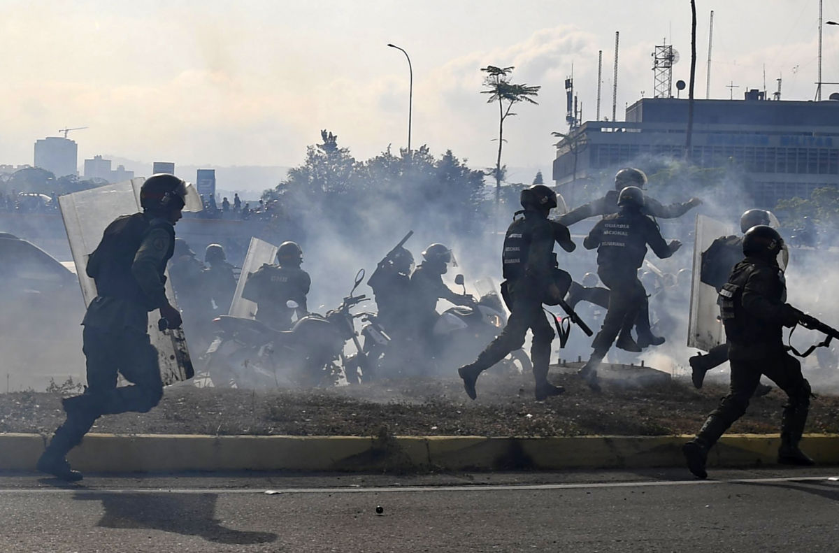 Soldiers dressed in black march through clouds of tear gas