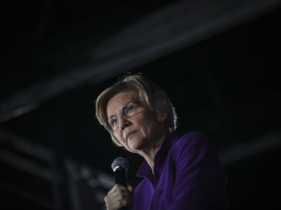 Elizabeth Warren holds a microphone in a darkened room