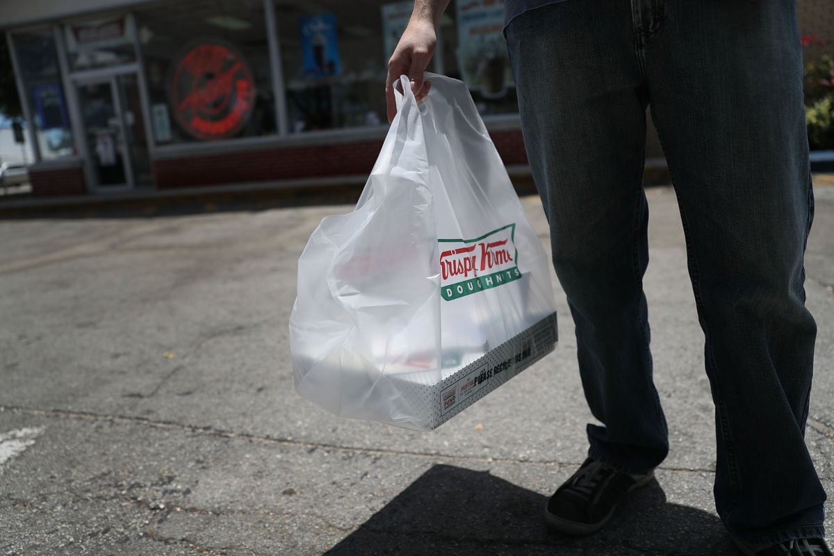 A man walks in a parking lot carrying a krispy kreme bag