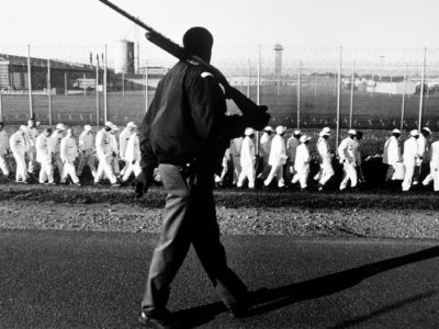 In a 1995 photo, prisoners on a chain gang are taken out for work detail by an armed guard at the Limestone Correctional Facility in Harvest, Alabama.
